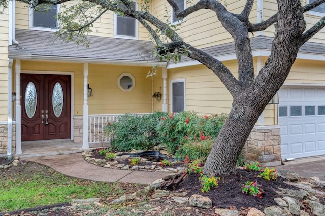 doorway to property with a garage, stone siding, a shingled roof, and covered porch