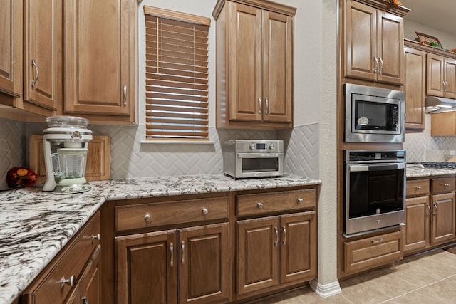 kitchen featuring light stone countertops, appliances with stainless steel finishes, light tile patterned floors, and backsplash