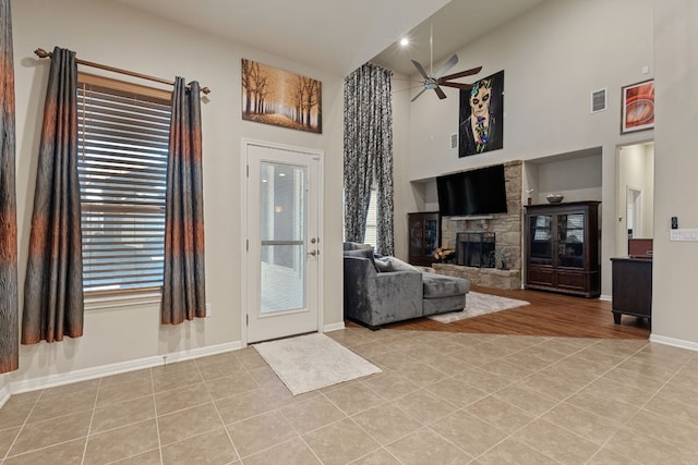 unfurnished living room with ceiling fan, a stone fireplace, a high ceiling, and light tile patterned flooring