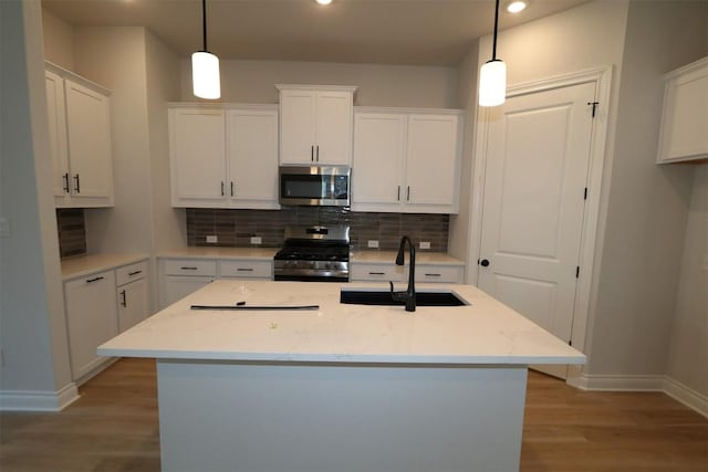 kitchen with stainless steel appliances, a sink, white cabinetry, light wood-style floors, and tasteful backsplash