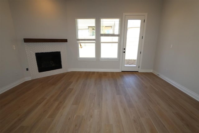 unfurnished living room with wood finished floors, a tile fireplace, and baseboards