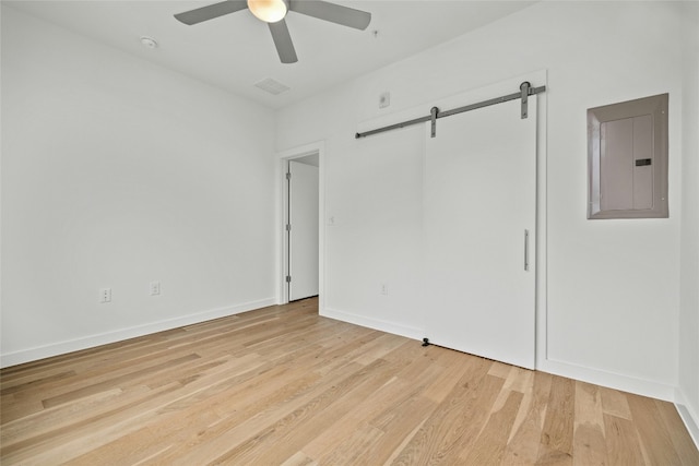 unfurnished room featuring light hardwood / wood-style flooring, electric panel, a barn door, and ceiling fan