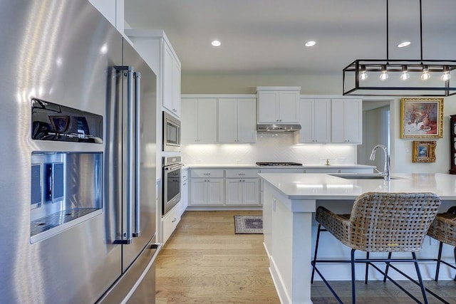 kitchen with sink, a center island with sink, appliances with stainless steel finishes, a kitchen breakfast bar, and white cabinets