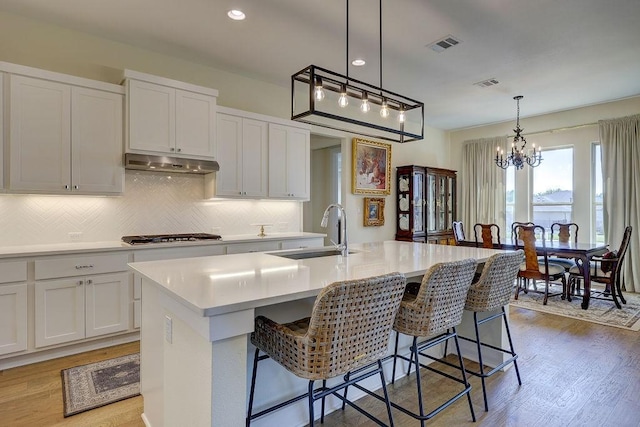 kitchen featuring a kitchen bar, stainless steel gas cooktop, sink, a center island with sink, and pendant lighting