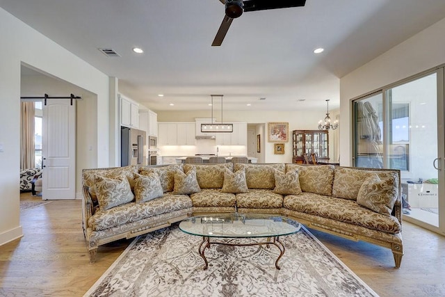 living room featuring a barn door, ceiling fan with notable chandelier, and light wood-type flooring