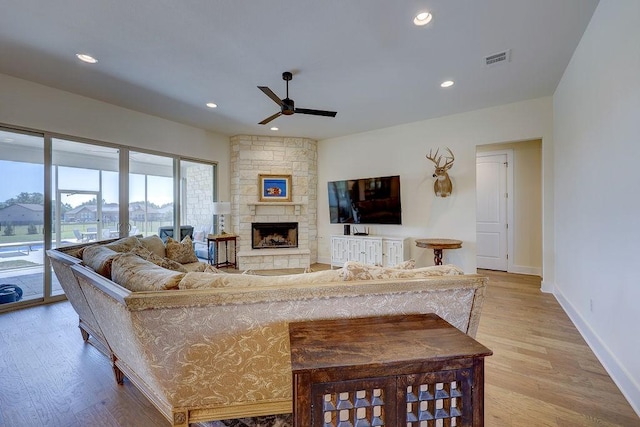 living room with a stone fireplace, ceiling fan, and light hardwood / wood-style flooring