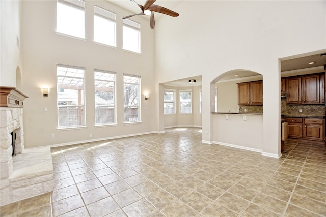 unfurnished living room with light tile patterned flooring, a stone fireplace, a healthy amount of sunlight, and ceiling fan