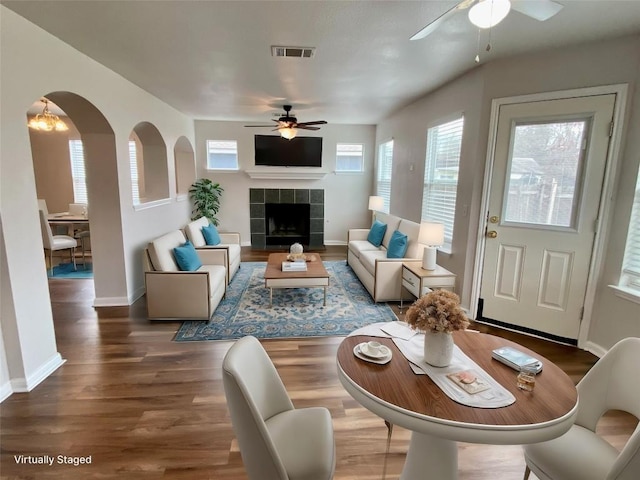 living room with wood-type flooring, a tiled fireplace, and ceiling fan with notable chandelier