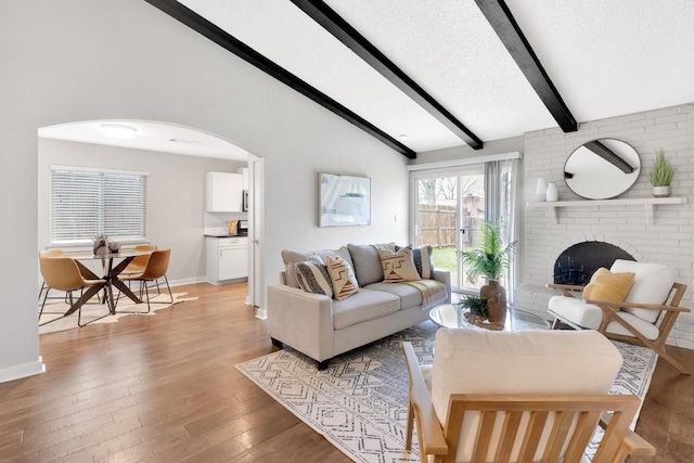 living room with vaulted ceiling with beams, a textured ceiling, a fireplace, and light hardwood / wood-style flooring