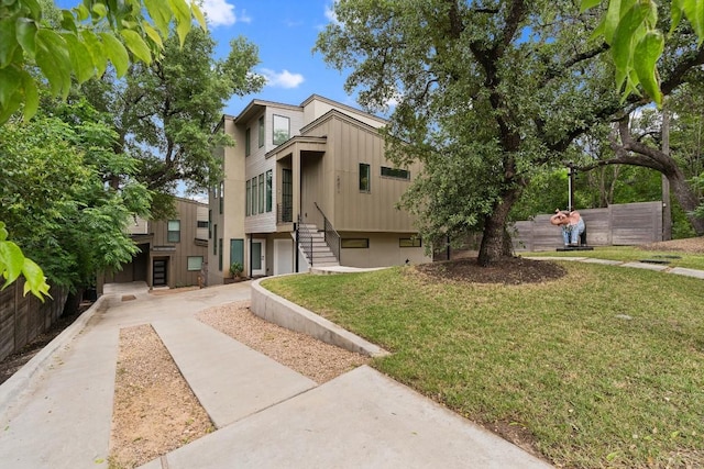 townhome / multi-family property with board and batten siding, a front yard, fence, and stairway