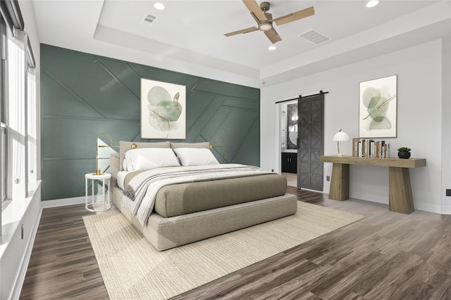 bedroom with a raised ceiling, a barn door, hardwood / wood-style flooring, and ceiling fan