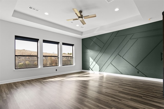 empty room featuring dark wood-type flooring, ceiling fan, and a tray ceiling