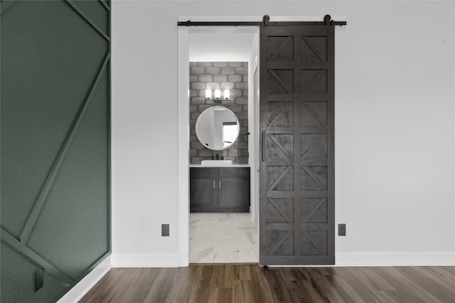 unfurnished bedroom featuring ensuite bath, sink, a barn door, and hardwood / wood-style floors