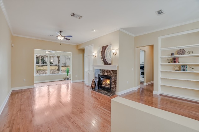 unfurnished living room with a premium fireplace, ceiling fan, ornamental molding, light hardwood / wood-style floors, and built in shelves