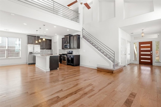 2211 Capulet St, Austin, TX 78741 - unfurnished living room featuring light wood-type flooring, baseboards, stairs, a ceiling fan, and a towering ceiling