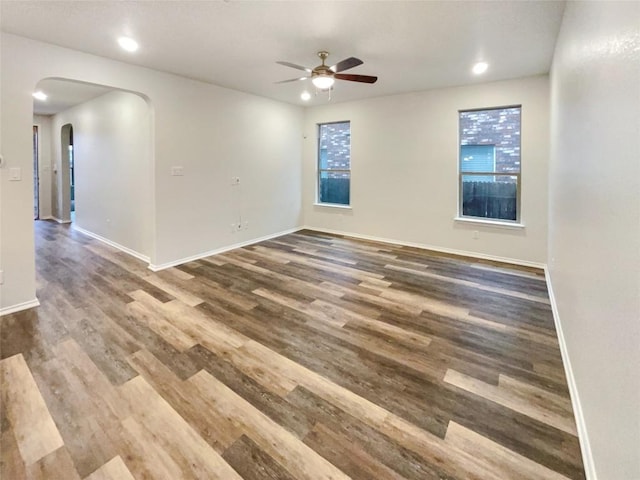 unfurnished room featuring baseboards, arched walkways, ceiling fan, and dark wood-style flooring