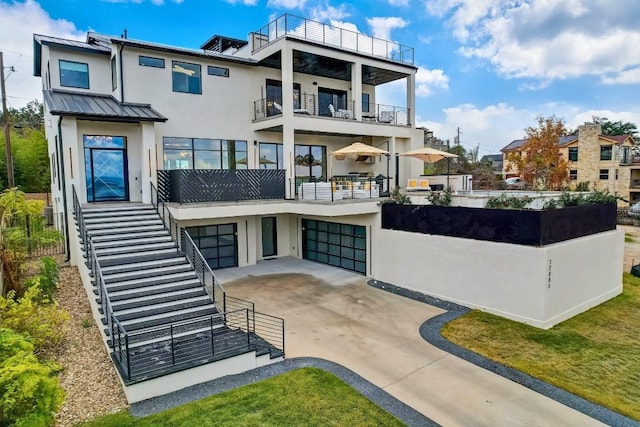 12885 Park Dr, Austin, TX 78732 - rear view of property with stucco siding, an attached garage, concrete driveway, a balcony, and a standing seam roof
