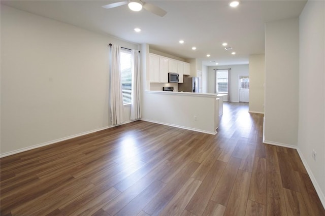 interior space with dark wood-type flooring, appliances with stainless steel finishes, kitchen peninsula, ceiling fan, and white cabinets