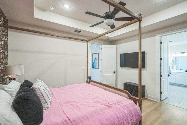 bedroom featuring ensuite bath, a textured ceiling, light hardwood / wood-style floors, and a tray ceiling