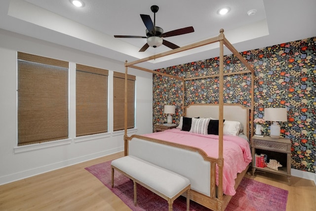 bedroom with hardwood / wood-style flooring, ceiling fan, and a raised ceiling