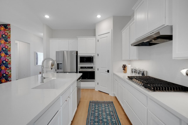 kitchen with stainless steel appliances, sink, exhaust hood, and white cabinets