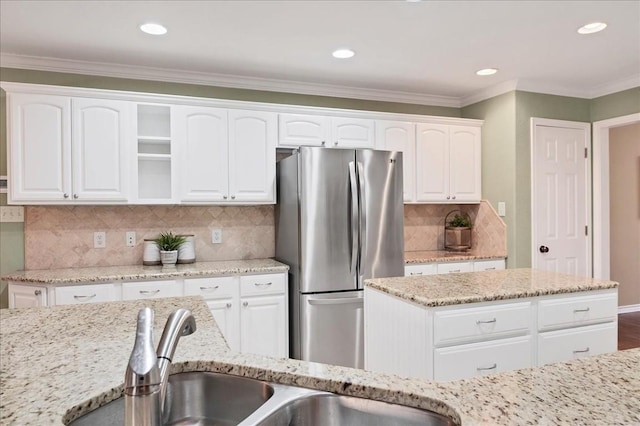 kitchen with crown molding, white cabinetry, light stone counters, and freestanding refrigerator