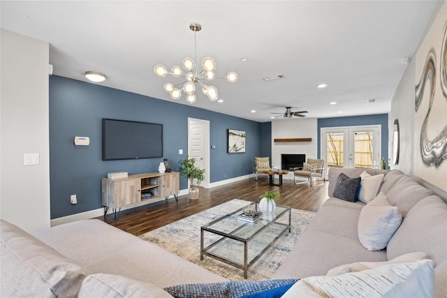 living room with dark wood-type flooring, a large fireplace, and ceiling fan with notable chandelier