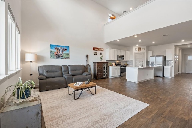 living room with a towering ceiling, a healthy amount of sunlight, dark hardwood / wood-style floors, and sink