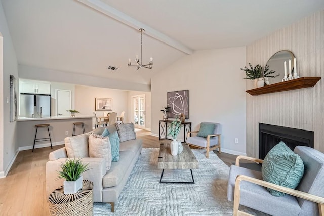 living room featuring an inviting chandelier, a fireplace, light hardwood / wood-style flooring, and lofted ceiling with beams