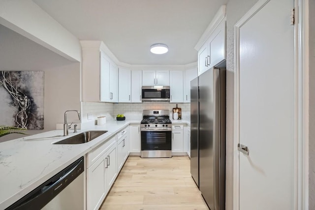 kitchen featuring sink, appliances with stainless steel finishes, white cabinetry, light stone countertops, and decorative backsplash