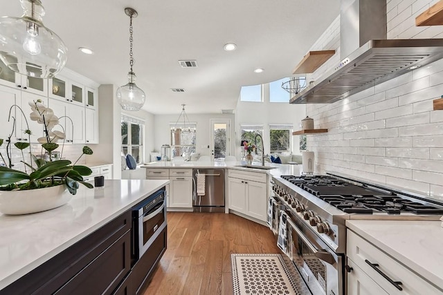 kitchen with white cabinetry, hanging light fixtures, stainless steel appliances, light hardwood / wood-style floors, and range hood