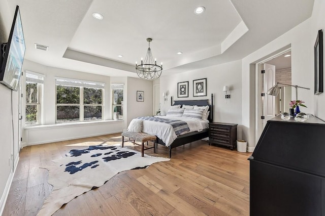 bedroom featuring a tray ceiling, light hardwood / wood-style floors, and a chandelier