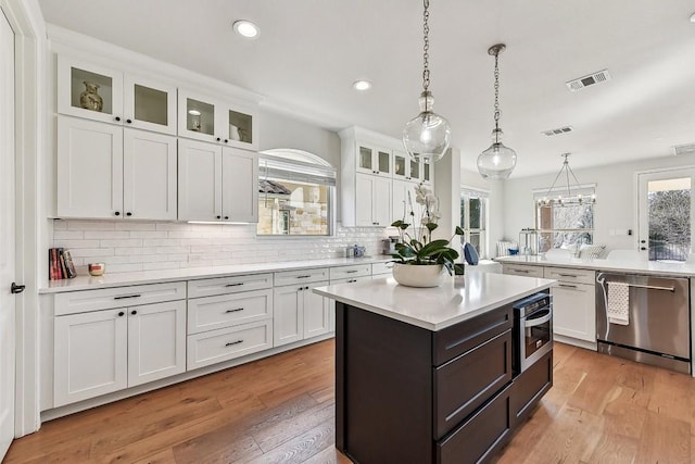 kitchen featuring stainless steel appliances, decorative light fixtures, light hardwood / wood-style floors, a center island, and white cabinetry