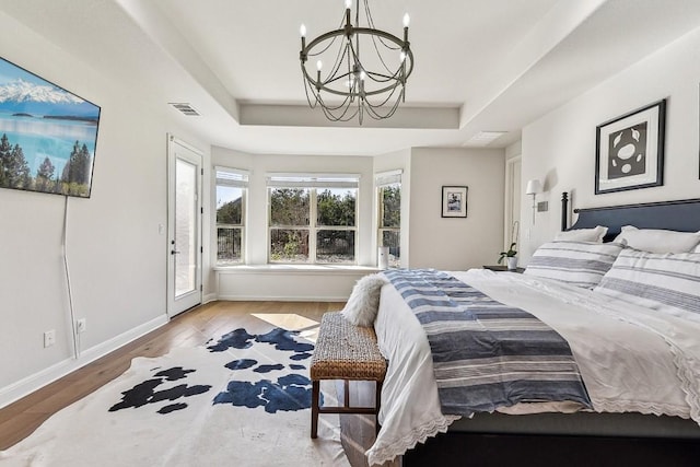 bedroom with light hardwood / wood-style flooring, access to outside, a notable chandelier, and a raised ceiling