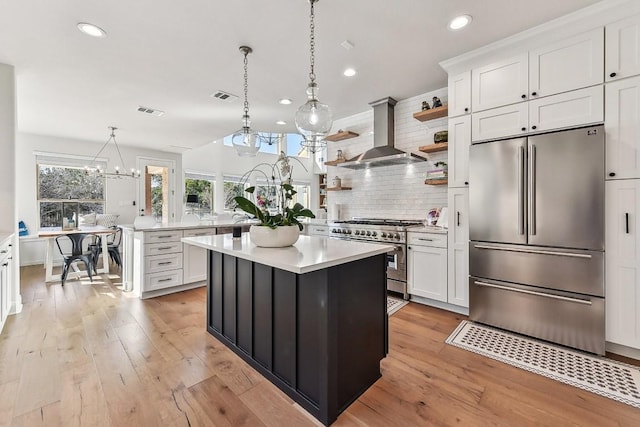 kitchen with white cabinetry, stainless steel appliances, a center island, decorative light fixtures, and wall chimney exhaust hood