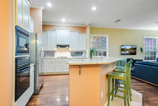 kitchen featuring light hardwood / wood-style flooring, a breakfast bar, black appliances, an island with sink, and white cabinets