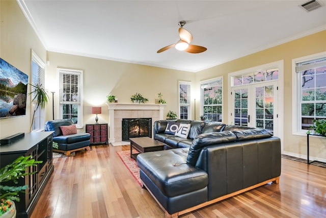 living room with french doors, crown molding, a tile fireplace, hardwood / wood-style flooring, and ceiling fan