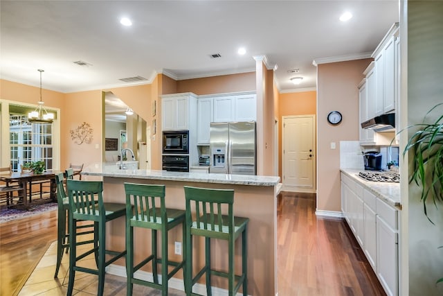 kitchen with light stone counters, a breakfast bar area, black appliances, and white cabinets