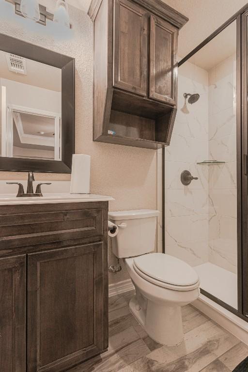 bathroom with vanity, wood-type flooring, tiled shower, and toilet