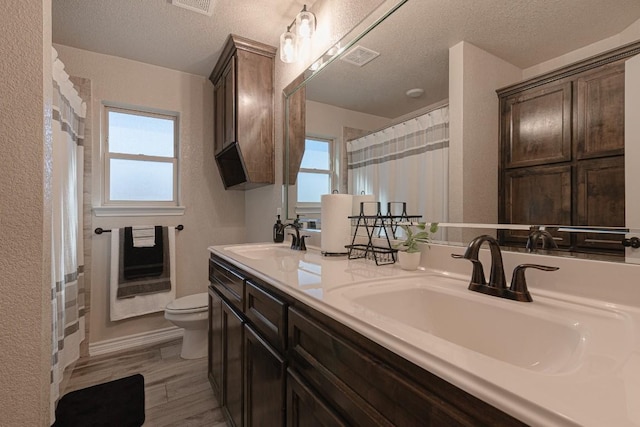 bathroom with heating unit, hardwood / wood-style flooring, vanity, toilet, and a textured ceiling