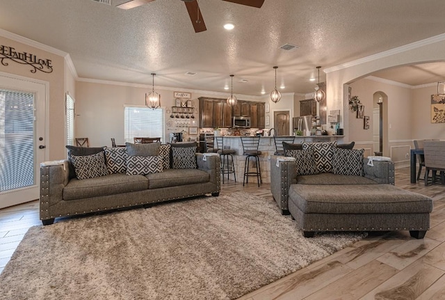 living room with ceiling fan, ornamental molding, a textured ceiling, and light wood-type flooring