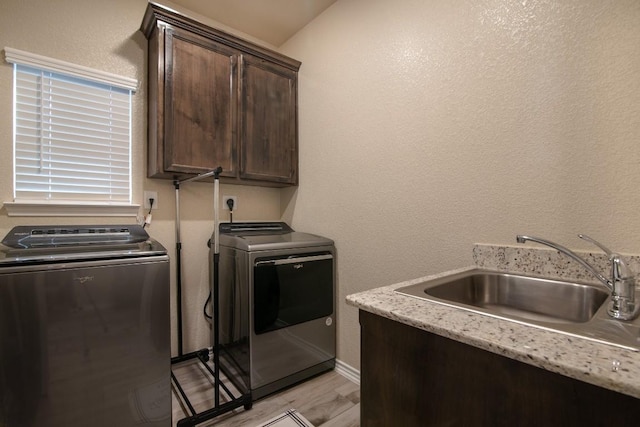 laundry room featuring cabinets, independent washer and dryer, sink, and light hardwood / wood-style flooring