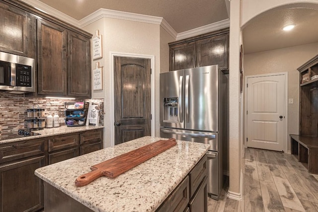 kitchen with stainless steel appliances, a center island, dark brown cabinetry, light stone countertops, and decorative backsplash