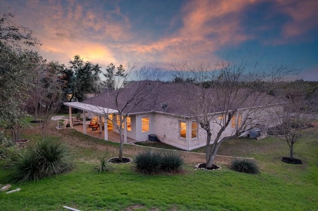 back house at dusk with a lawn and a patio area