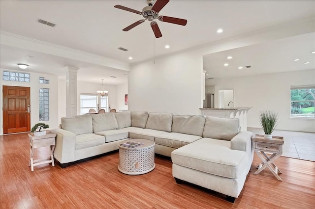 living room featuring decorative columns, light hardwood / wood-style floors, and ceiling fan with notable chandelier