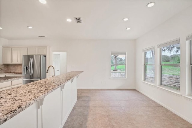 kitchen featuring stainless steel refrigerator with ice dispenser, light stone countertops, light tile patterned floors, white cabinets, and decorative backsplash