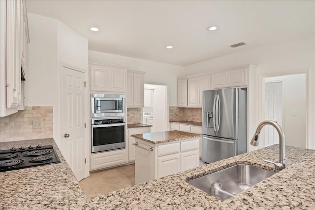 kitchen featuring appliances with stainless steel finishes, light stone counters, a kitchen island, sink, and white cabinetry