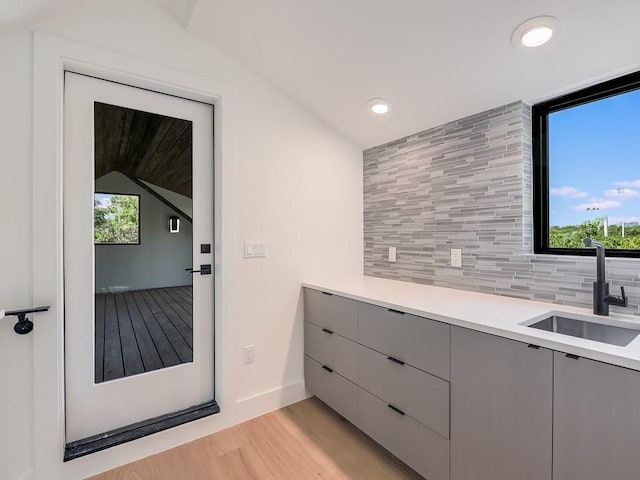 interior space with sink, gray cabinets, tasteful backsplash, light hardwood / wood-style floors, and vaulted ceiling