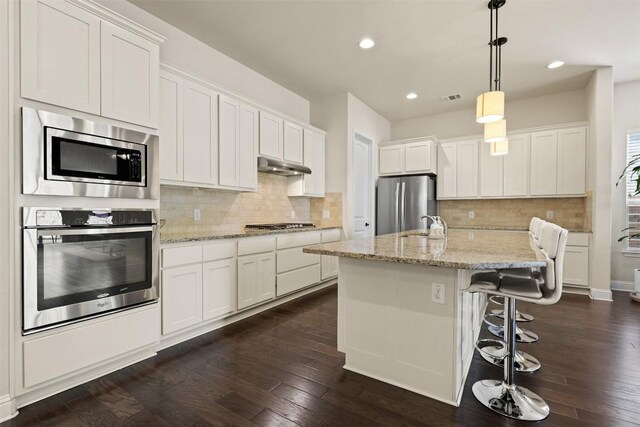 kitchen with stainless steel appliances, hanging light fixtures, a kitchen island with sink, and white cabinets