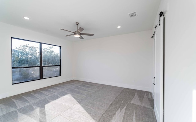 unfurnished room featuring ceiling fan, carpet flooring, and a barn door